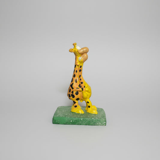 Toy giraffe on a white sheet of paper held by a person against a wooden surface.